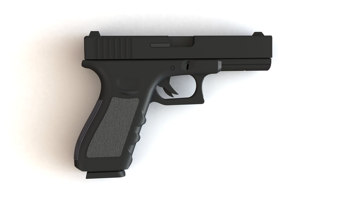 A pistol isolated on white. The pistol has a loaded magazine of bullets and is places on a white surface.