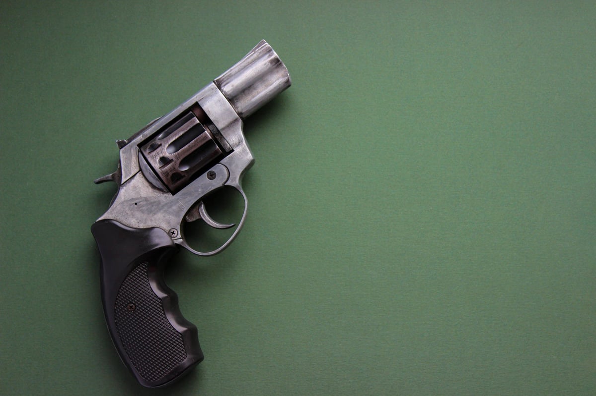 Top view of a compact snub-nose revolver placed on green paper with copy space. Clean studio lighting for security, crime or self-defense topics.